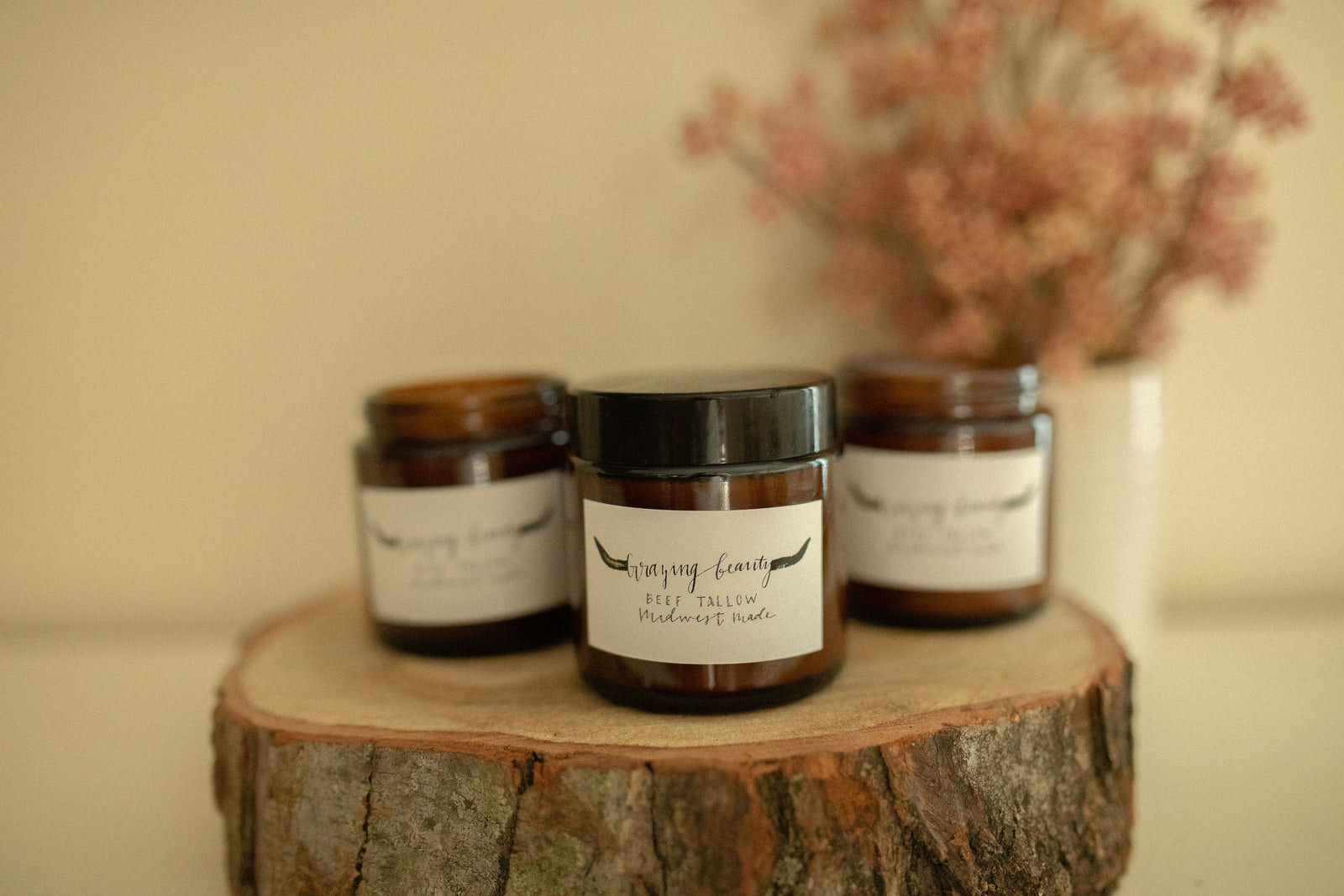 Grazing Beauty tallow balm jars styled on a wood stump